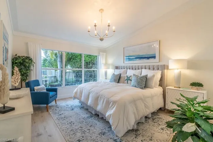 Primary bedroom suite is spacious and inviting, featuring a coastal-style chandelier, lofted ceiling, crown molding, and custom baseboard, a lage walk in closet and deep linen closet.