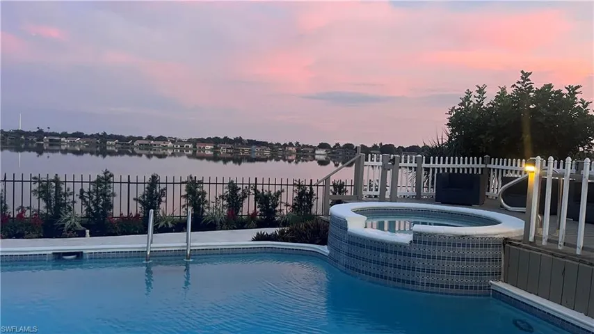 Pool at dusk with an in ground hot tub and a water view