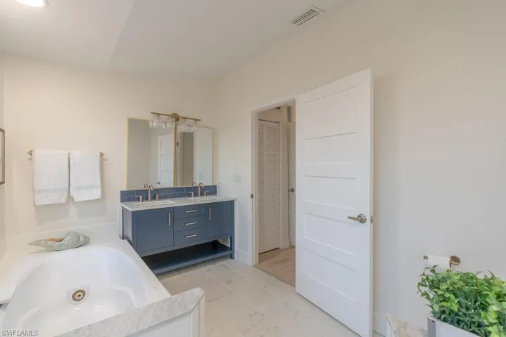 Primary bathroom has a navy nautical style flair, with tile floors, a jacuzzi soaking tub, dual sink vanity with custom glass backsplash tile, modern coastal vanity lights and gold fixtures. Large walk-in shower is separate from the tub.