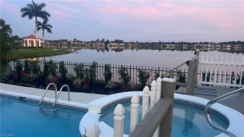 Pool at dusk featuring a water view and a hot tub