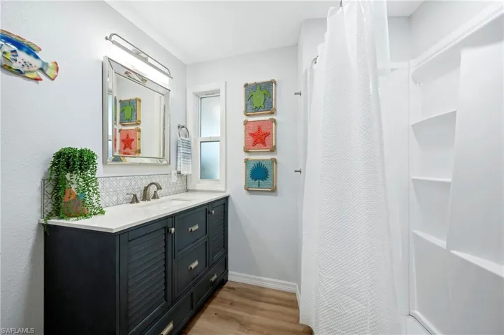 Full bathroom with tasteful backsplash, vanity, baseboards, a shower with curtain, and wood finished floors