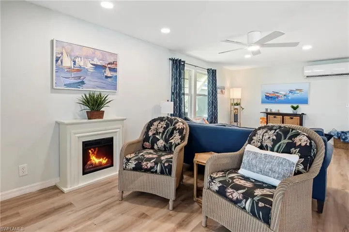 Living area featuring a warm lit fireplace, a wall mounted air conditioner, recessed lighting, ceiling fan, and wood finished floors