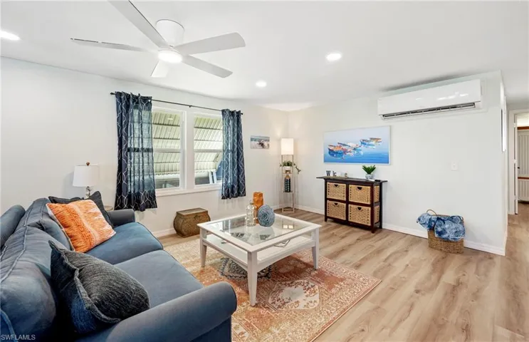 Living room featuring an AC wall unit, baseboards, recessed lighting, light wood-style flooring, and ceiling fan