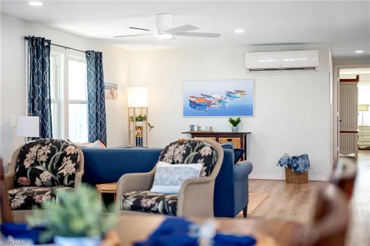 Living room with wood finished floors, a wall mounted air conditioner, a ceiling fan, and plenty of natural light