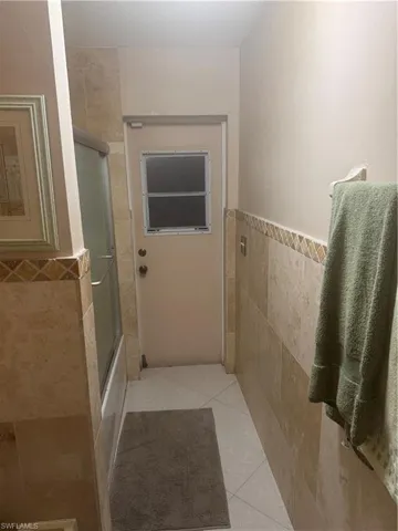 Bathroom featuring tile walls, tile patterned floors, combined bath / shower with glass door, and a wainscoted wall