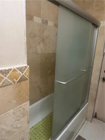 Bathroom with bath / shower combo with glass door and tile patterned floors