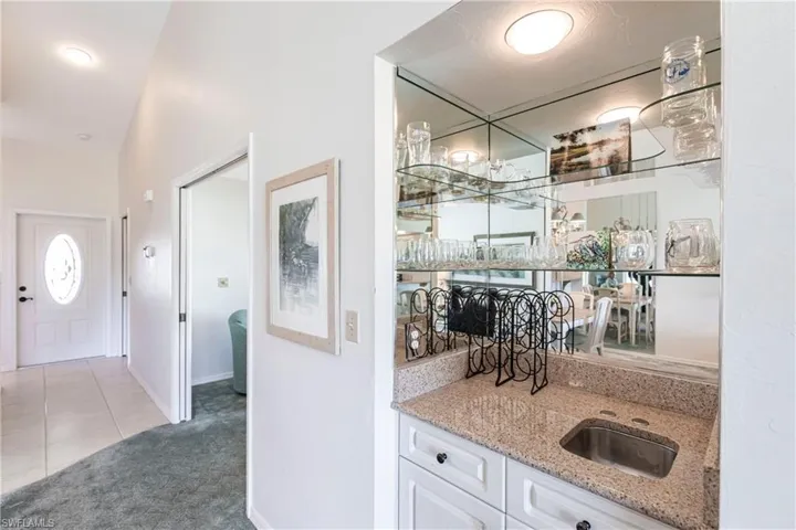 Bar with sink, light carpet, white cabinets, and light stone counters