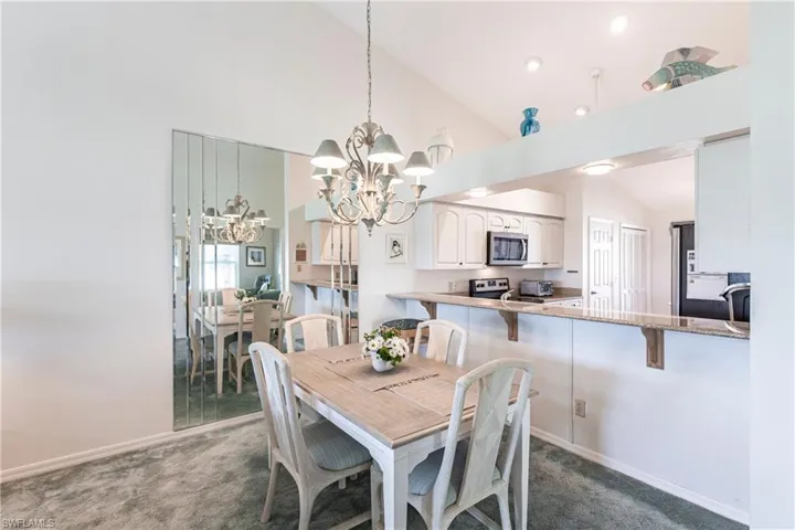 Carpeted dining space featuring a notable chandelier and high vaulted ceiling