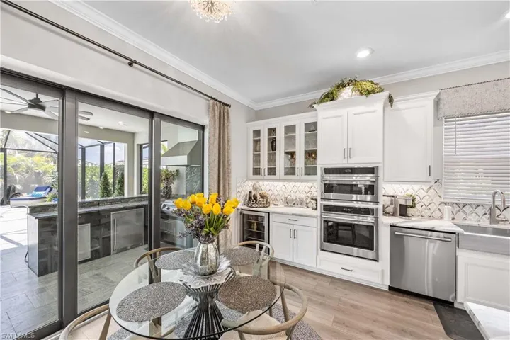 Kitchen featuring white cabinets, wine cooler, ornamental molding, light hardwood / wood-style flooring, and appliances with stainless steel finishes
