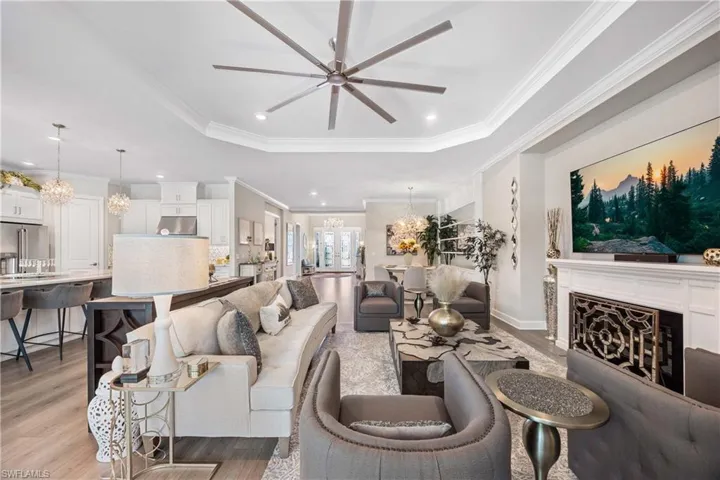 Living room with ceiling fan with notable chandelier, crown molding, a tray ceiling, and light hardwood / wood-style flooring