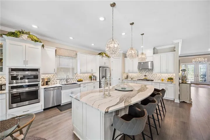 Kitchen featuring white cabinets, a kitchen island, exhaust hood, stainless steel appliances, and a notable chandelier