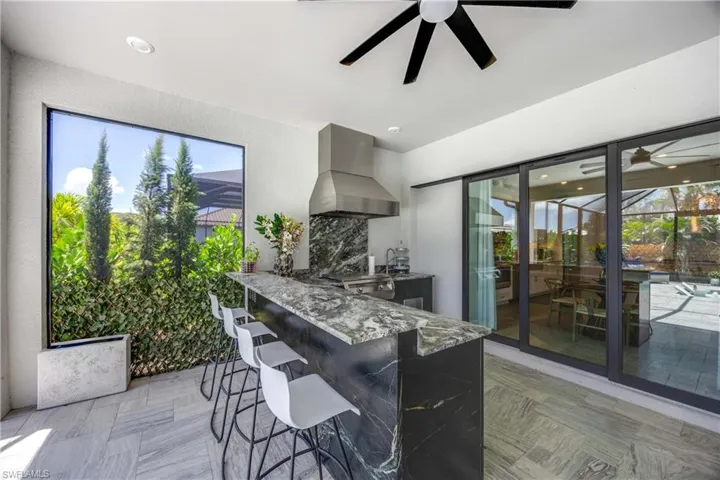 Kitchen featuring a kitchen breakfast bar, wall chimney exhaust hood, kitchen peninsula, stone counters, and ceiling fan