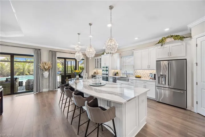 Kitchen featuring white cabinetry, a kitchen island, stainless steel appliances, light wood-type flooring, and decorative light fixtures