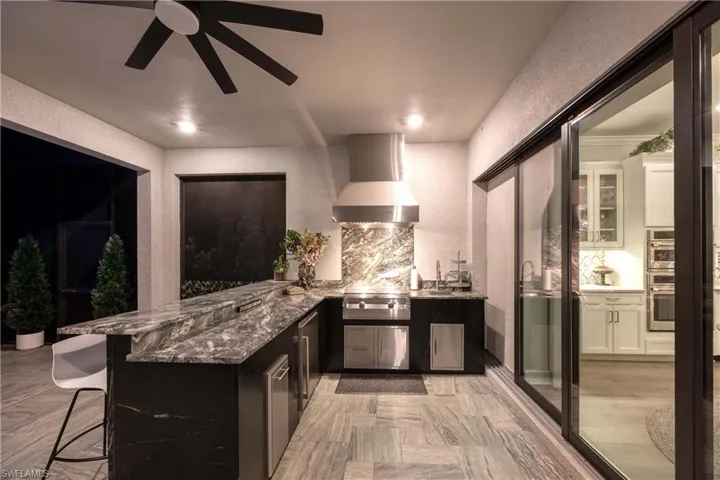 Bar featuring ceiling fan, wall chimney exhaust hood, backsplash, white cabinetry, and dark stone counters