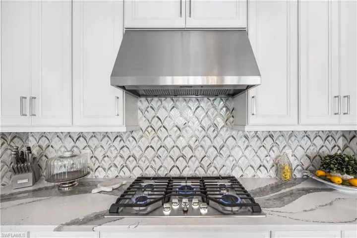 Kitchen featuring stainless steel gas stovetop, wall chimney exhaust hood, and white cabinetry