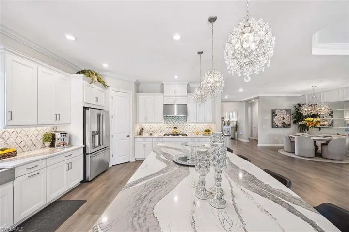 Kitchen featuring light stone counters, decorative light fixtures, stainless steel appliances, and white cabinets