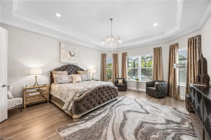 Bedroom with wood-type flooring, a tray ceiling, ornamental molding, and multiple windows
