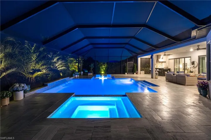 Pool at night featuring glass enclosure, a patio, an in ground hot tub, an outdoor living space, and ceiling fan