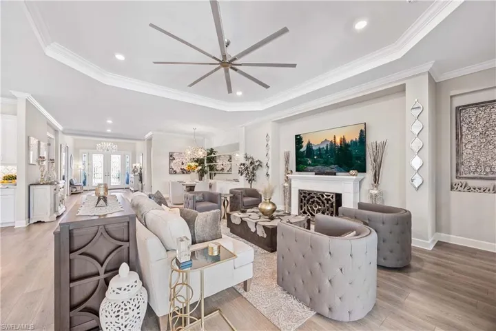 Living room with ceiling fan with notable chandelier, light hardwood / wood-style floors, a raised ceiling, and ornamental molding