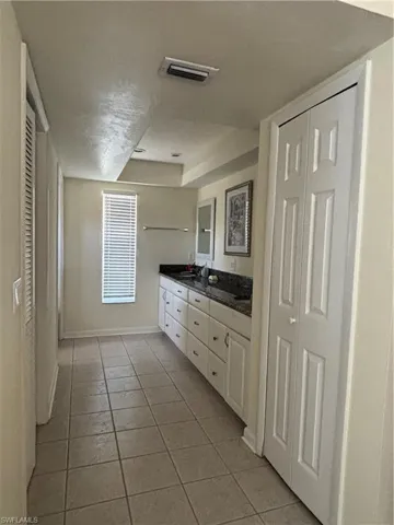 Bathroom featuring a double vanity with white cabinetry and dark countertops, tiled flooring, and a window with blinds