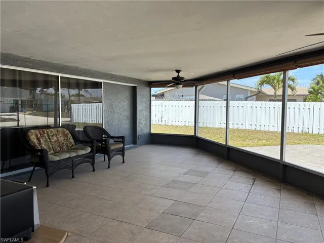 Expansive screened-in lanai featuring tiled flooring, a ceiling fan, and large windows looking out to the yard with a white privacy fence