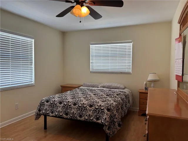 Bedroom featuring light-colored walls, wood flooring, and windows with blinds