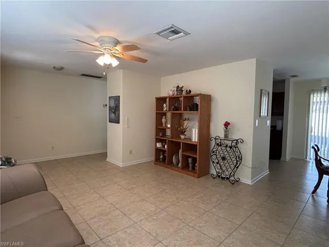 This living area features neutral-toned walls, tile flooring, and a ceiling fan with integrated lighting