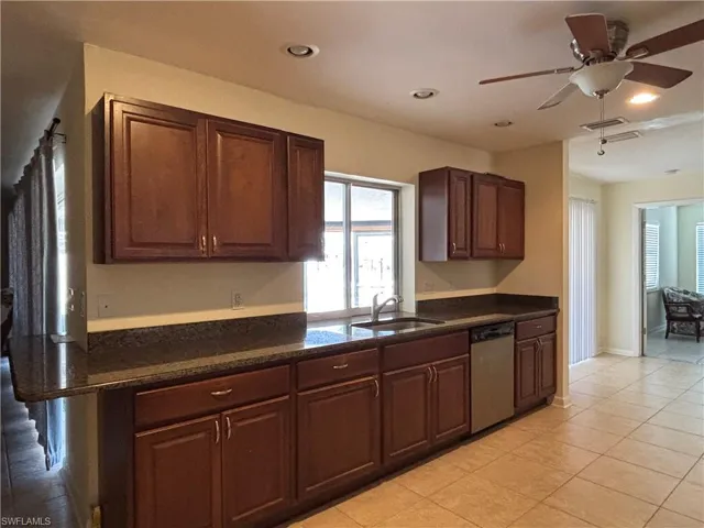 Kitchen featuring dark wood cabinetry, a stainless steel dishwasher, a window over the sink, and recessed lighting