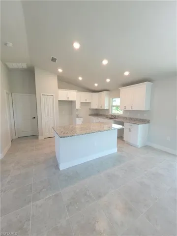 Kitchen featuring white cabinetry, a kitchen island, light stone counters, and lofted ceiling