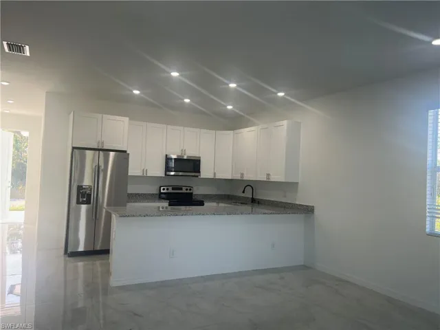 Kitchen with white cabinetry, light stone counters, kitchen peninsula, and stainless steel appliances