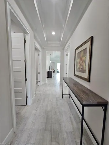 Hallway featuring light wood-type flooring, crown molding, a tray ceiling, and recessed lighting