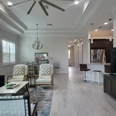 Living area with hanging lights, light wood finished floors, a ceiling fan, and plenty of natural light