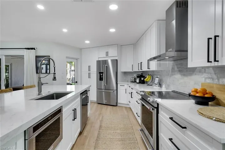 Kitchen featuring a sink, tasteful backsplash, light wood-type flooring, stainless steel appliances, and wall chimney range hood