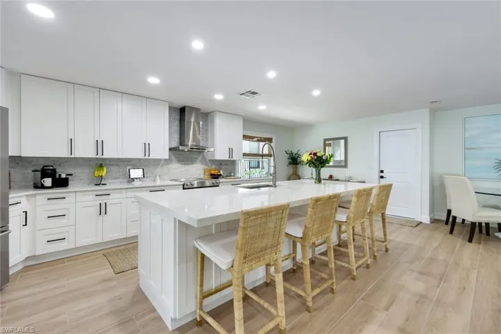 Kitchen with a sink, wall chimney exhaust hood, tasteful backsplash, stove, and a kitchen island with sink
