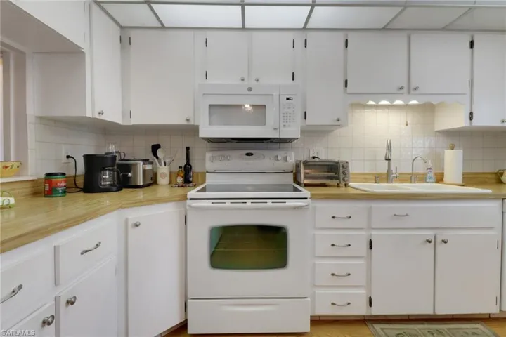 Kitchen with tasteful backsplash, white appliances, and white cabinetry