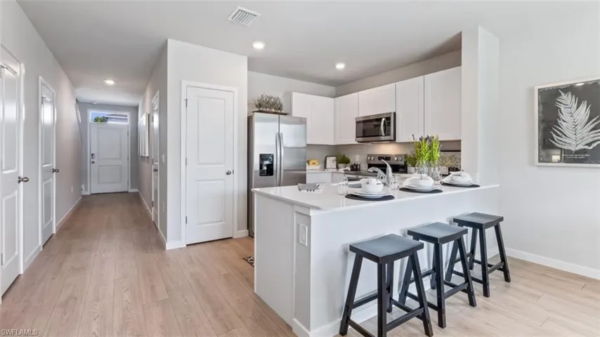 Model home. Kitchen featuring white cabinets, a kitchen breakfast bar, stainless steel appliances, light wood-style flooring, and a peninsula