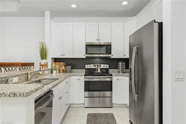 Kitchen featuring granite counters, white cabinetry, stainless steel appliances, and white tile floors