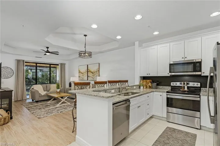 Kitchen with a raised ceiling, white cabinets, kitchen peninsula, and appliances with stainless steel finishes
