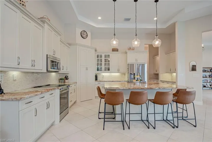 Kitchen featuring stainless steel appliances, light stone countertops, a breakfast bar area, decorative backsplash, and a high tray ceiling