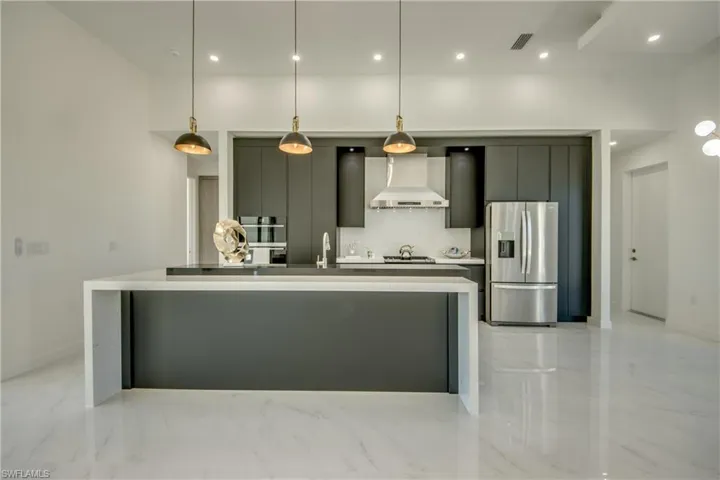 Kitchen featuring sink, wall chimney exhaust hood, hanging light fixtures, stainless steel appliances, and a large island with sink