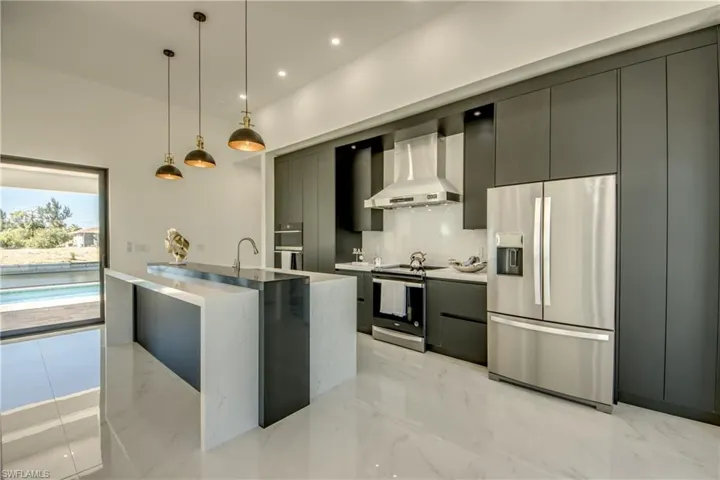 Kitchen with decorative backsplash, appliances with stainless steel finishes, wall chimney exhaust hood, sink, and decorative light fixtures