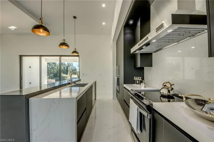Kitchen featuring stainless steel electric range oven, sink, wall chimney exhaust hood, light stone counters, and pendant lighting