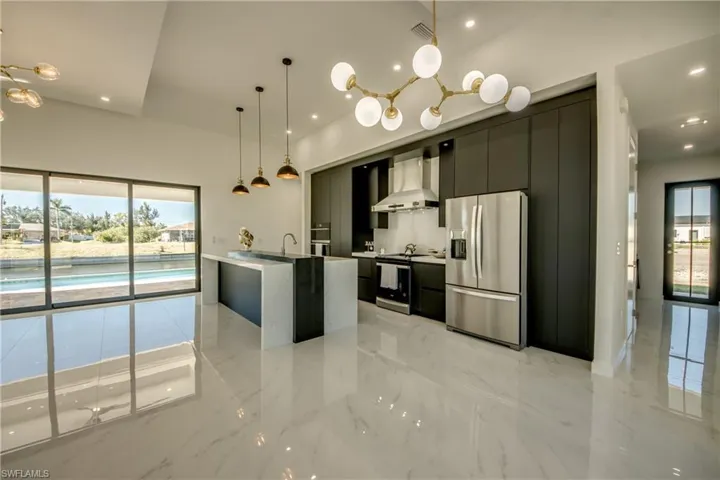 Kitchen with wall chimney range hood, plenty of natural light, hanging light fixtures, and stainless steel refrigerator with ice dispenser