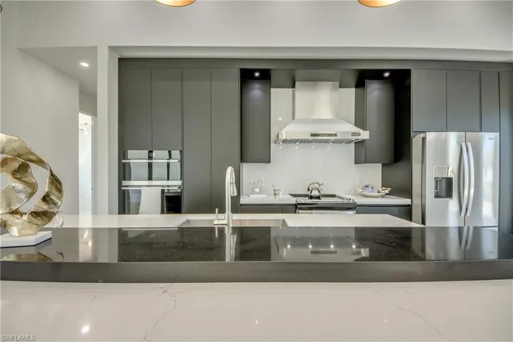 Kitchen with decorative backsplash, dark stone counters, wall chimney exhaust hood, gray cabinetry, and stainless steel appliances