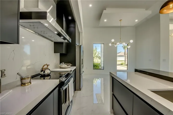 Kitchen with pendant lighting,  exhaust hood, appliances with stainless steel finishes, tasteful backsplash, and a chandelier