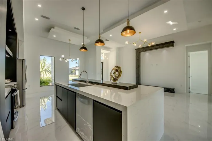 Kitchen with a large island with sink, decorative light fixtures, appliances with stainless steel finishes, and sink
