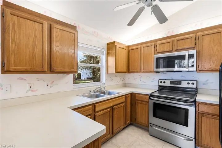 Kitchen featuring sink, vaulted ceiling, appliances, and ceiling fan