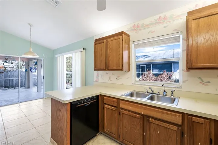 Kitchen featuring sink, hanging light fixtures, black dishwasher, vaulted ceiling, and kitchen peninsula