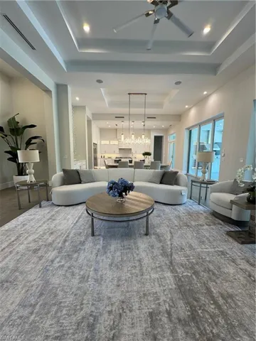Living area with a tray ceiling, recessed lighting, ceiling fan with notable chandelier, and visible vents