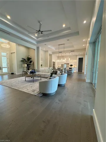 Unfurnished living room featuring dark wood finished floors, a tray ceiling, and ceiling fan with notable chandelier